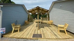A covered outdoor deck with wooden chairs and a table, surrounded by two buildings with siding.