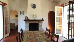 Ein Essbereich mit Kamin, einem Tisch mit bunten Tischdecken und Blick ins Freie durch eine Glastür.
