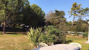Eine Terrasse im Freien mit einem runden Tisch und vier Stühlen, umgeben von Grünpflanzen und Bäumen.