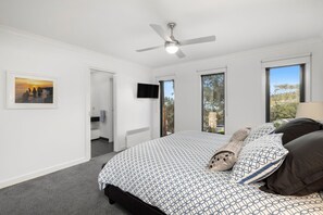 A bedroom with a bed, a ceiling fan, a TV, and a window with a view.