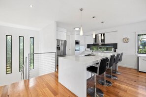 A modern kitchen with a central island, stainless steel appliances, and a view of greenery outside.