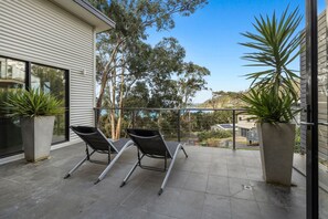 A balcony with two lounge chairs, potted plants, and a view of trees and buildings.