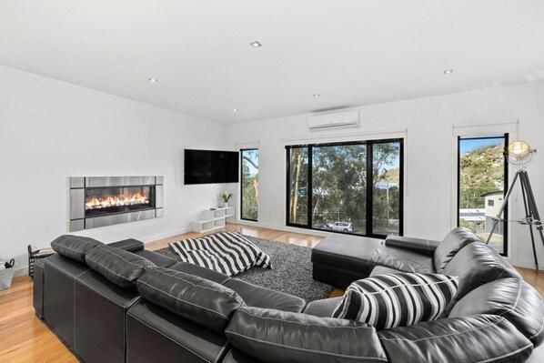 A modern living room with a fireplace, leather sofas, and large windows.