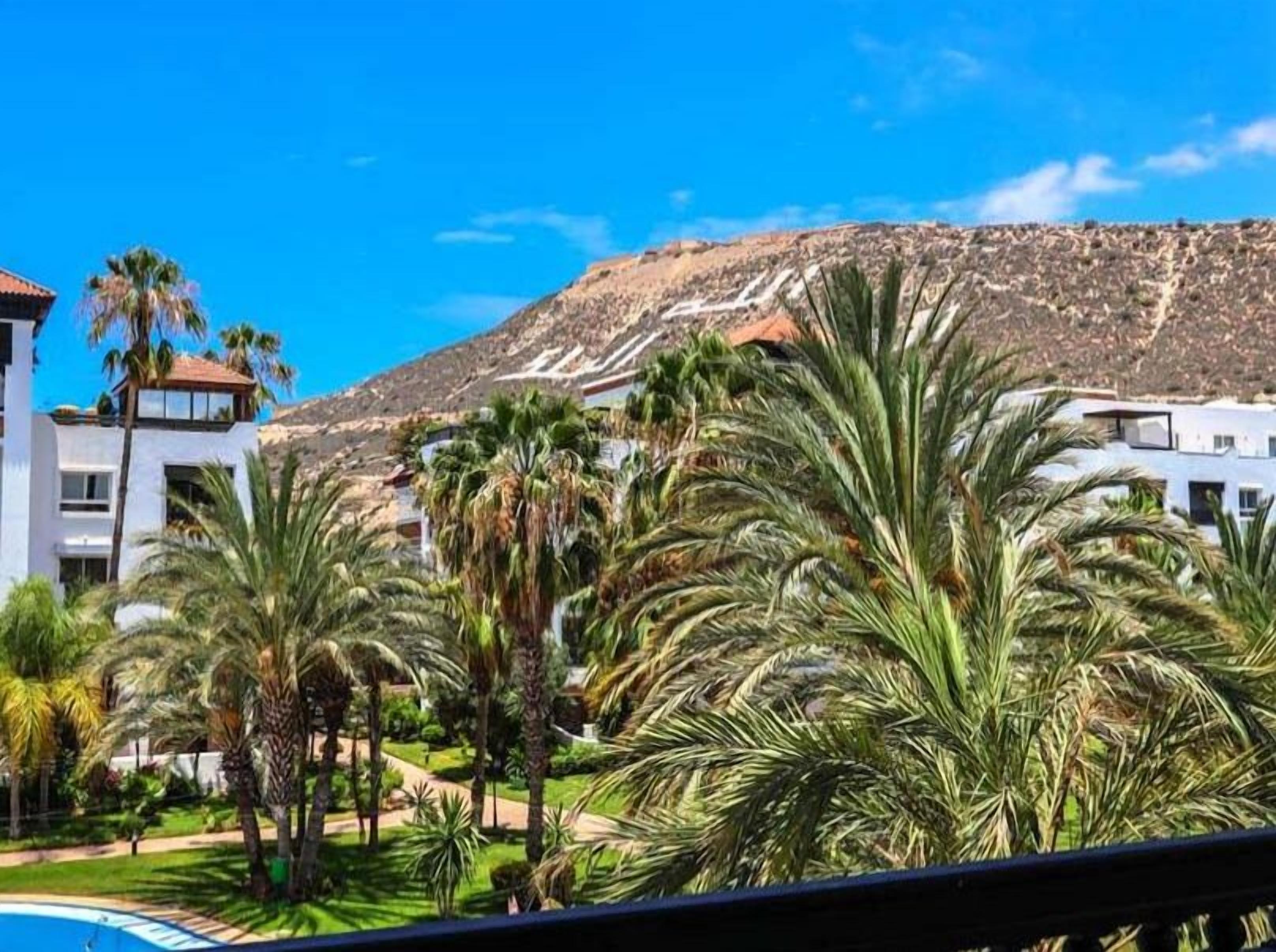 A resort with a pool, palm trees, and a mountainous backdrop.