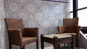 A wicker chair and a small table with a patterned tabletop, positioned near a window with a patterned wall in the background. - Residence Marina Agadir 4821 (Agadir)