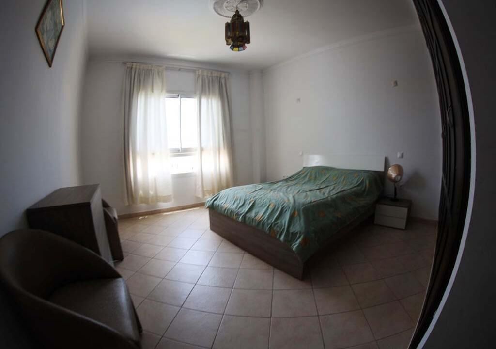 Un dormitorio con cama, una silla, una mesita de noche y una ventana con cortinas.