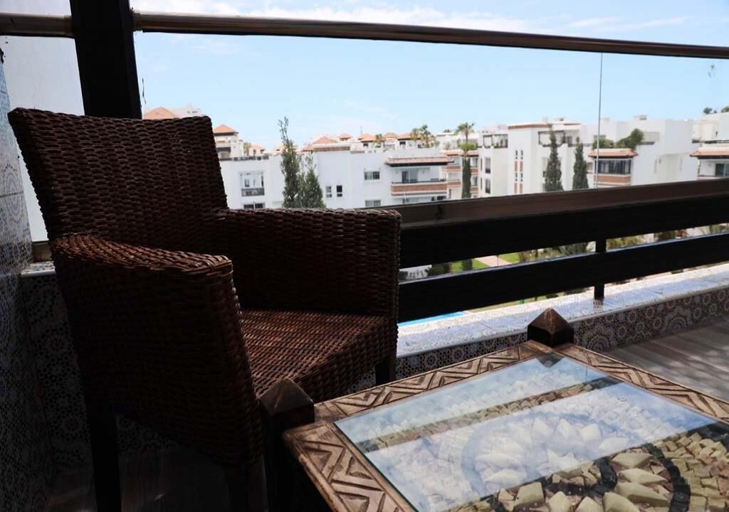 Un balcón con mobiliario de mimbre y una mesa con estampado, con vistas a una zona residencial.