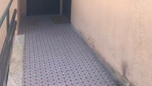 A narrow hallway with patterned flooring leading to a door. There is a window with a curtain on the right wall.
