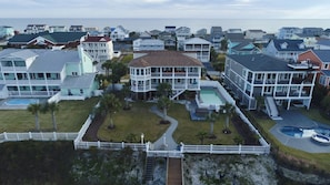 A coastal residential area with multiple two-story houses, a central building with a swimming pool, and a white picket fence. - Holden Beach masterpiece loaded with 6 bedrooms, 6.5 baths and stunning views (Holden Beach)