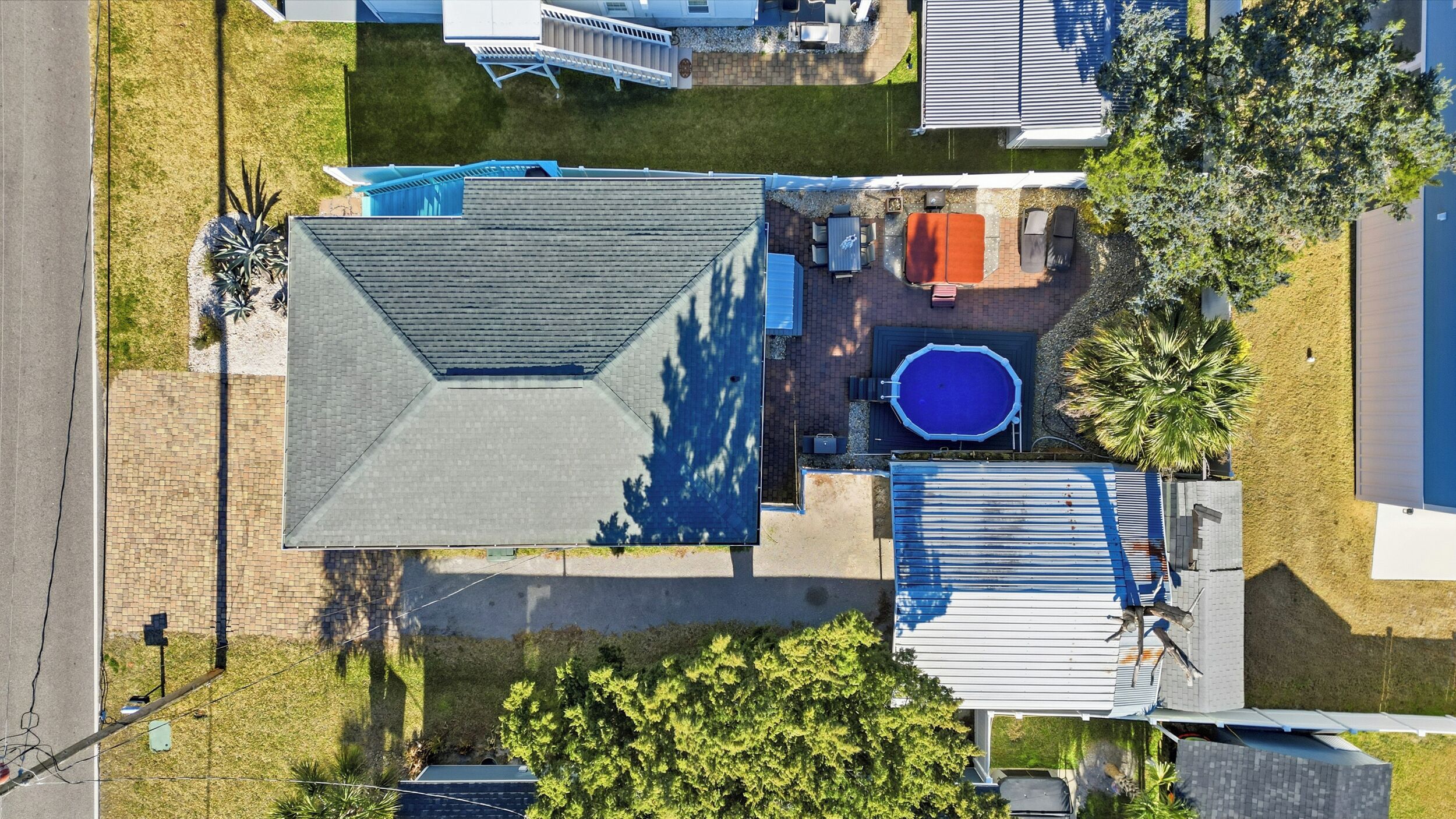 An aerial view of a residential property with a large house, a swimming pool, and a covered patio area.