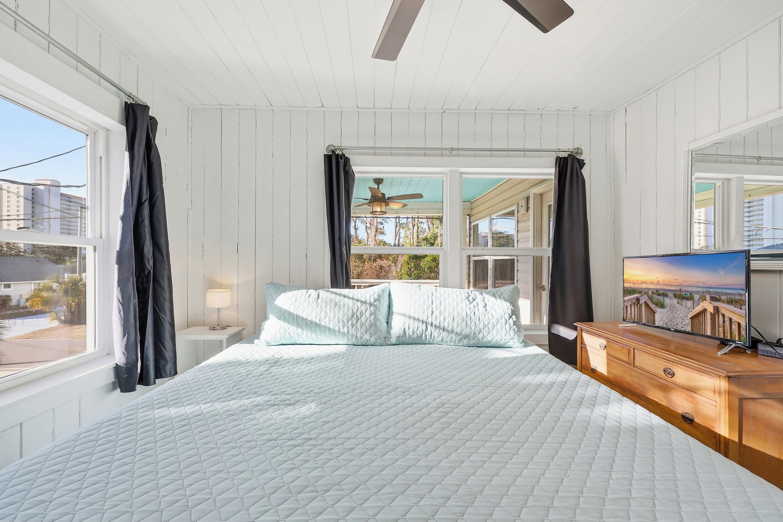 A bedroom with a bed, a dresser, a TV, and a window with curtains.