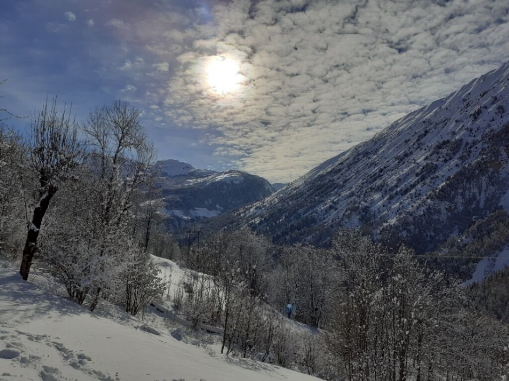 A snowy mountain landscape with a clear sky and a sun shining through clouds.