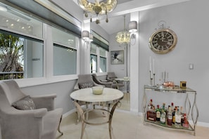 Una sala de estar moderna con una mesa redonda, asientos cómodos, un reloj decorativo y un aparador de vidrio con botellas.