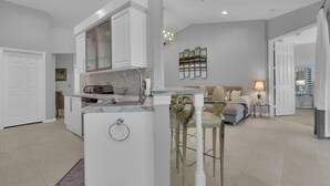 Una cocina moderna con una isla central, un área de comedor con un sofá y sillas, y una sala de estar con un sofá y una lámpara.