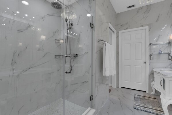 Un baño moderno con cabina de ducha de vidrio, paredes de mármol y una puerta blanca.