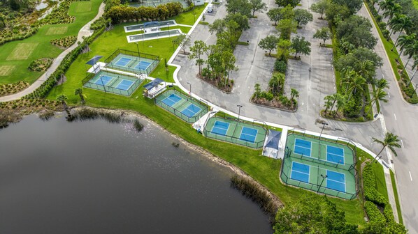 Vista aérea de una propiedad con varias canchas de tenis, un estacionamiento y una masa de agua.