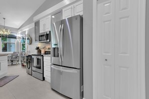 Une cuisine moderne dotée d’appareils électroménagers en acier inoxydable, de meubles blancs et d’un lustre.