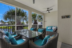 A sunlit patio with wicker furniture, a glass table, and a ceiling fan.