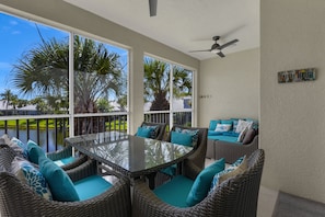A covered patio with wicker furniture, a glass table, and a ceiling fan. - HAWK'S NEST 202 - Luxurious Remodeled Fiddler's Creek Coach Home (Naples)