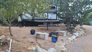 Un véhicule récréatif (VR) est stationné sur une surface de gravier, agrémentée de plantes en pot et d’un banc en pierre.