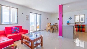 A spacious living area with a red sofa, a glass coffee table, and a dining area with wooden chairs. - Casa Perla Suite 1 a 2 Bdrm Caribbean Oceanfront Condo w/ dipping pool (Isla Mujeres)