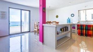 A modern kitchen with a central island, a dining area with chairs, and a view of the sea through large windows. - Casa Perla Suite 1 a 2 Bdrm Caribbean Oceanfront Condo w/ dipping pool (Isla Mujeres)