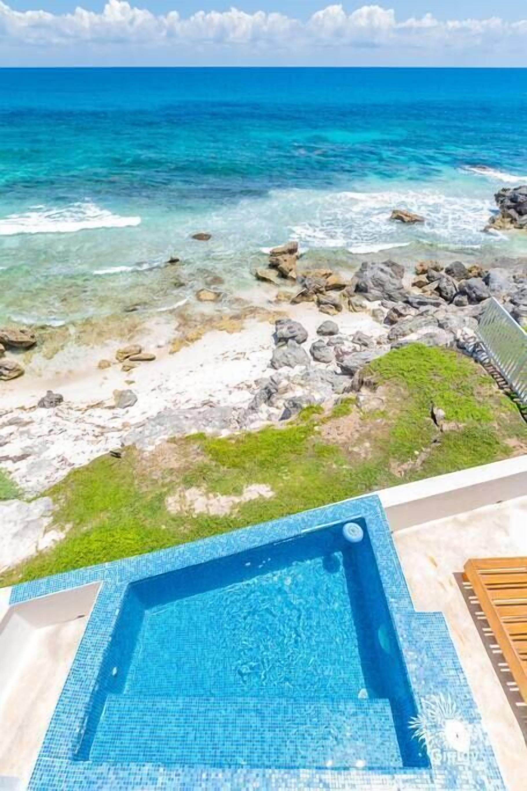 A swimming pool with clear blue water, surrounded by a rocky shoreline and a view of the ocean.
