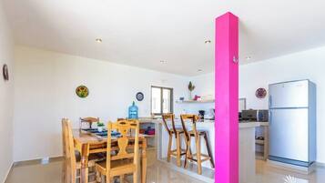 A modern kitchen with wooden chairs, a dining table, and a bright pink accent wall.