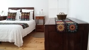 Un dormitorio ordenado con cama, mesita de noche, una pequeña mesa y un banco.