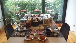 Una mesa de desayuno servida con diversos alimentos y bebidas, rodeada de sillas, con vista a la vegetación exterior.