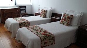 Two single beds with floral bedspreads, a wooden dresser, a chair, and a nightstand with a lamp. - Casa 45 (Porto)