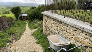 Ein Kiesweg führt zu einer Steinmauer mit einer Holzbeschreibung und einem Metallzaun.