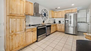 A modern kitchen with wooden cabinets, stainless steel appliances, and a tiled floor. - 12 Park Rd - Octopus Oasis (Hilton Head Island)
