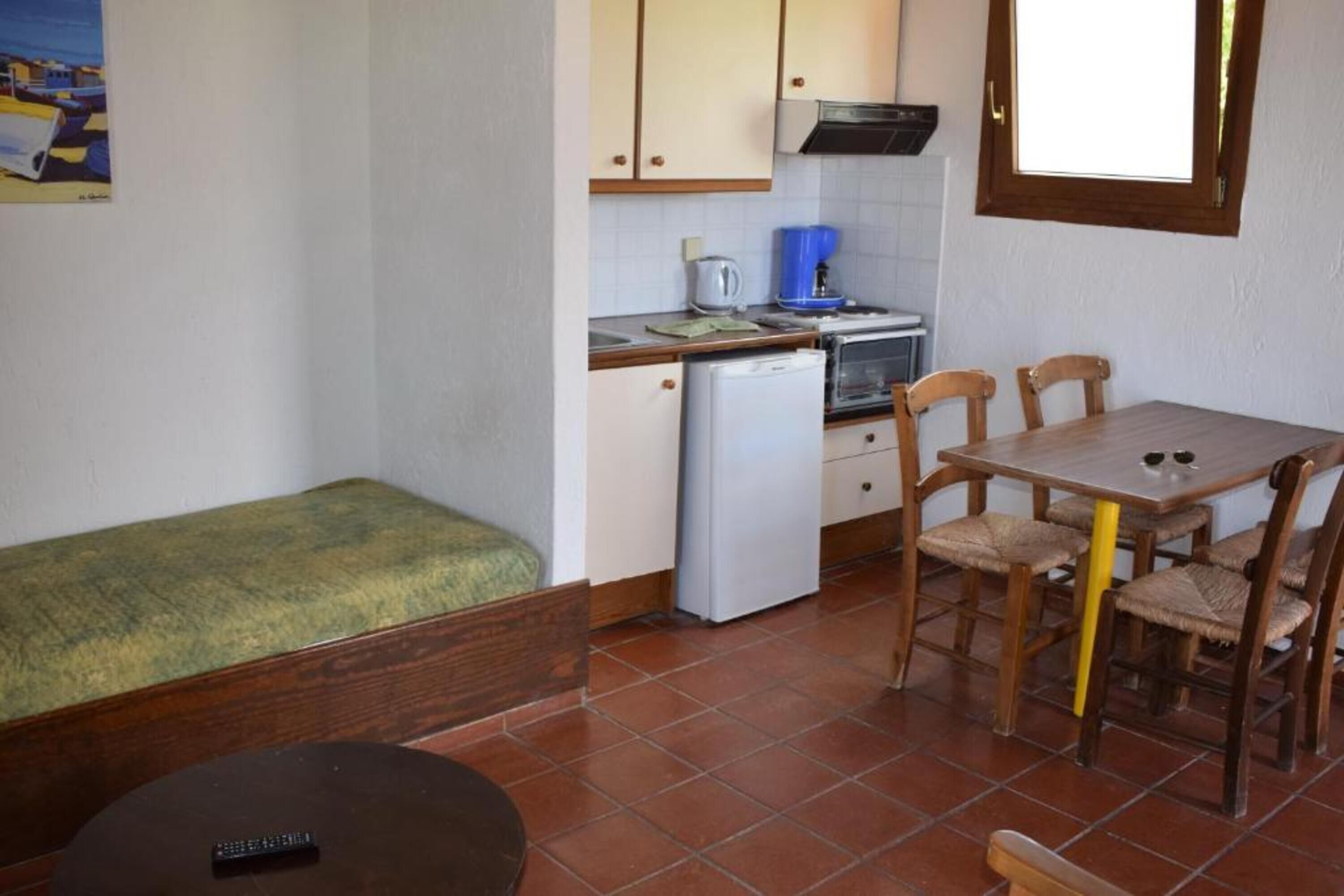 A compact kitchen with a dining area, a small refrigerator, and a single bed.