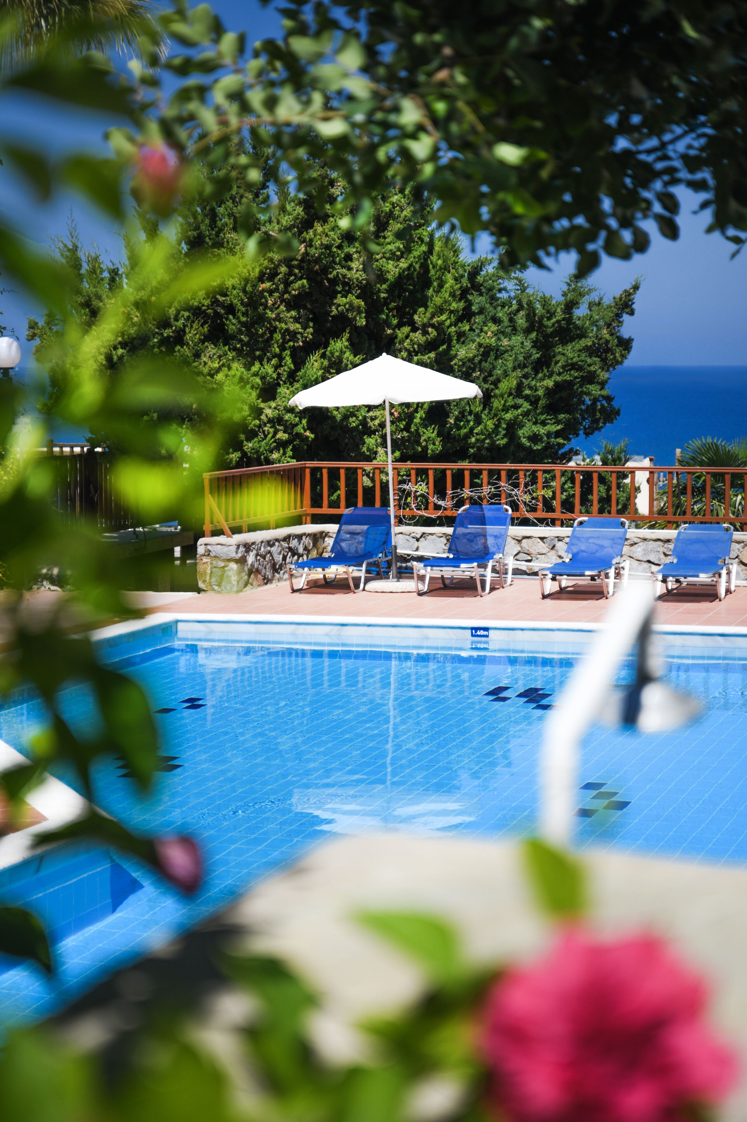 A swimming pool with blue water, surrounded by blue lounge chairs and a white umbrella.