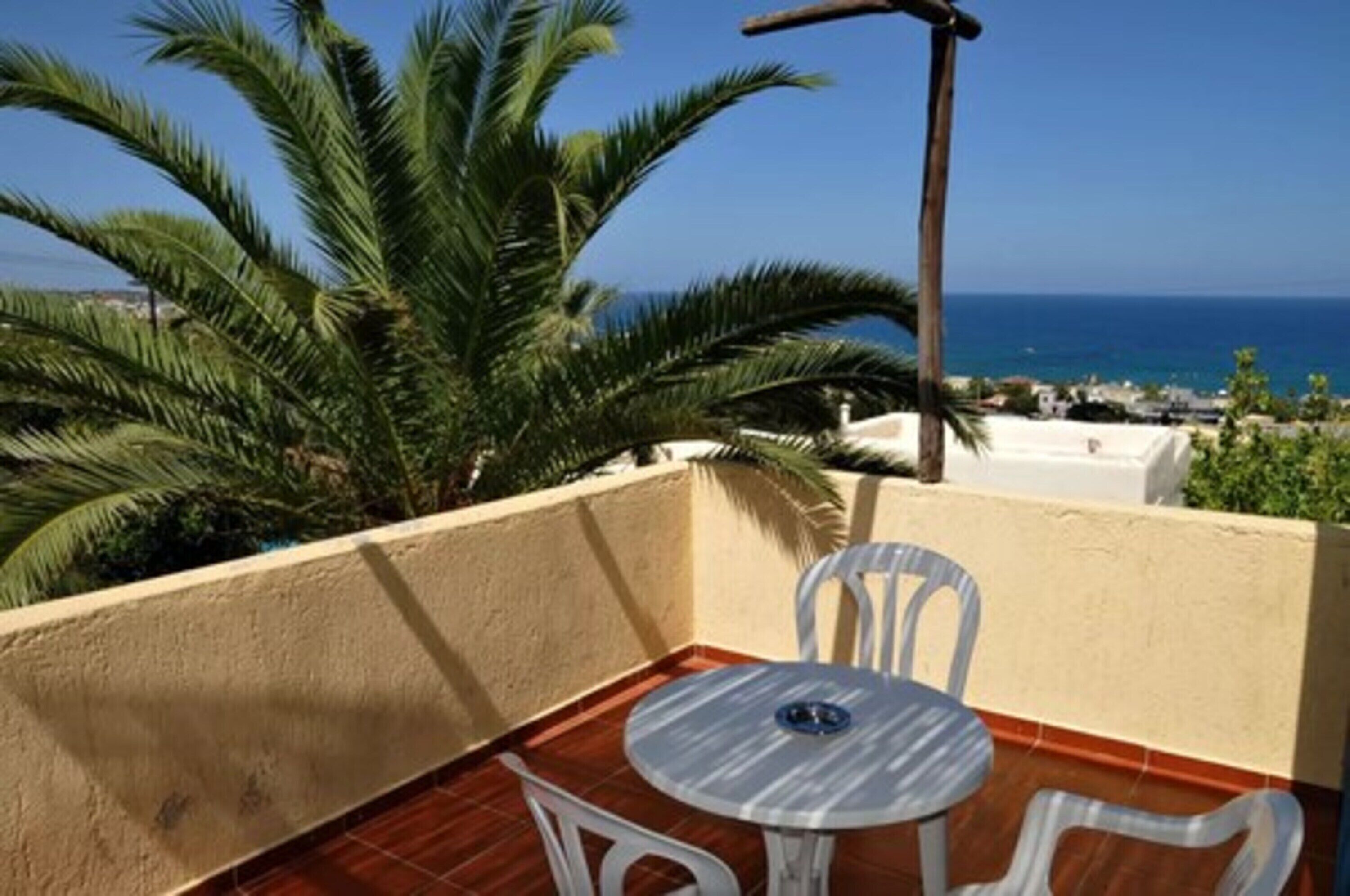 Een balkon met een tafel en stoelen, met uitzicht op de kust, palmbomen en de zee.