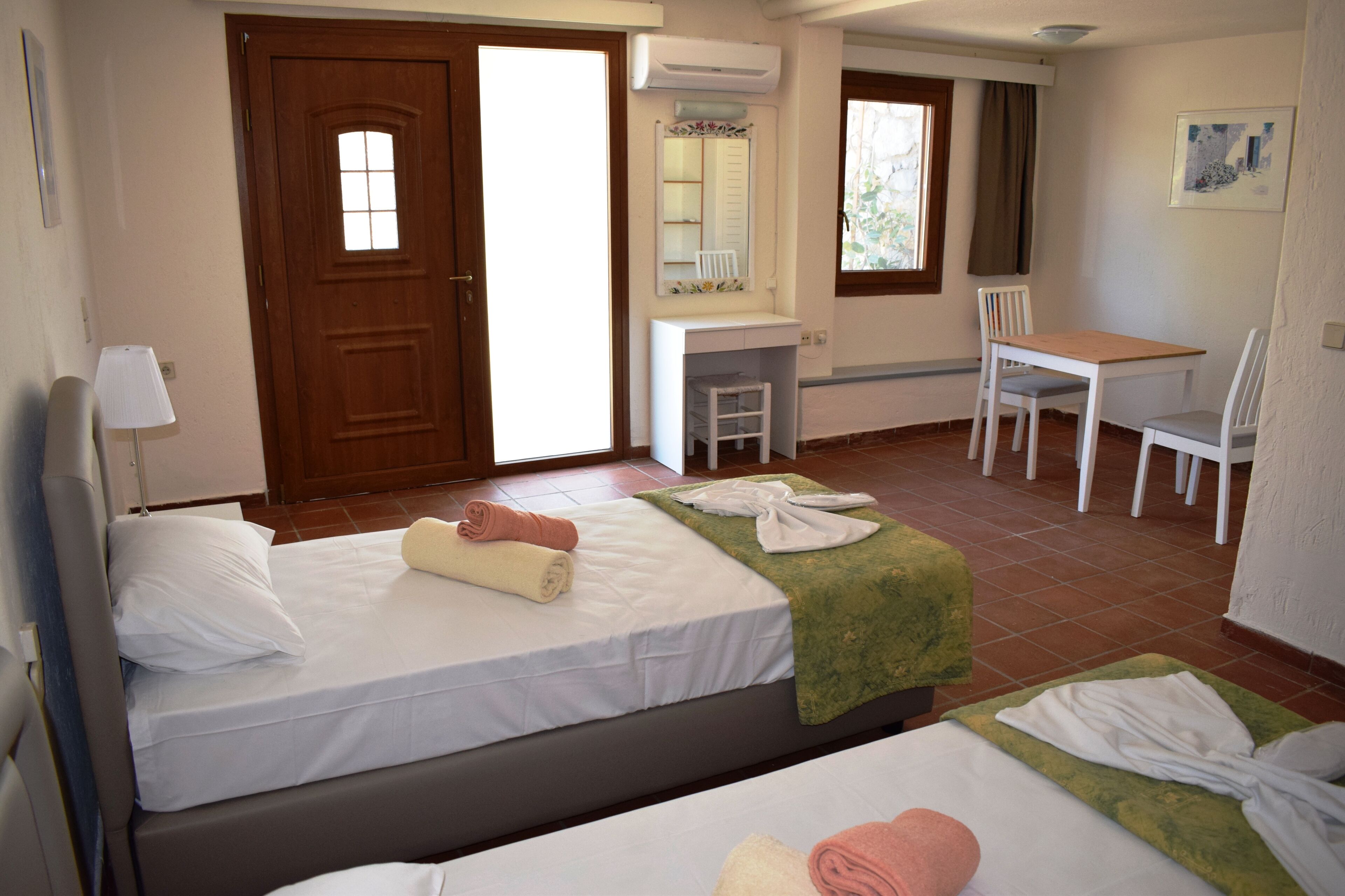 Una habitación de hotel con dos camas, un escritorio, una silla, un espejo y una ventana.