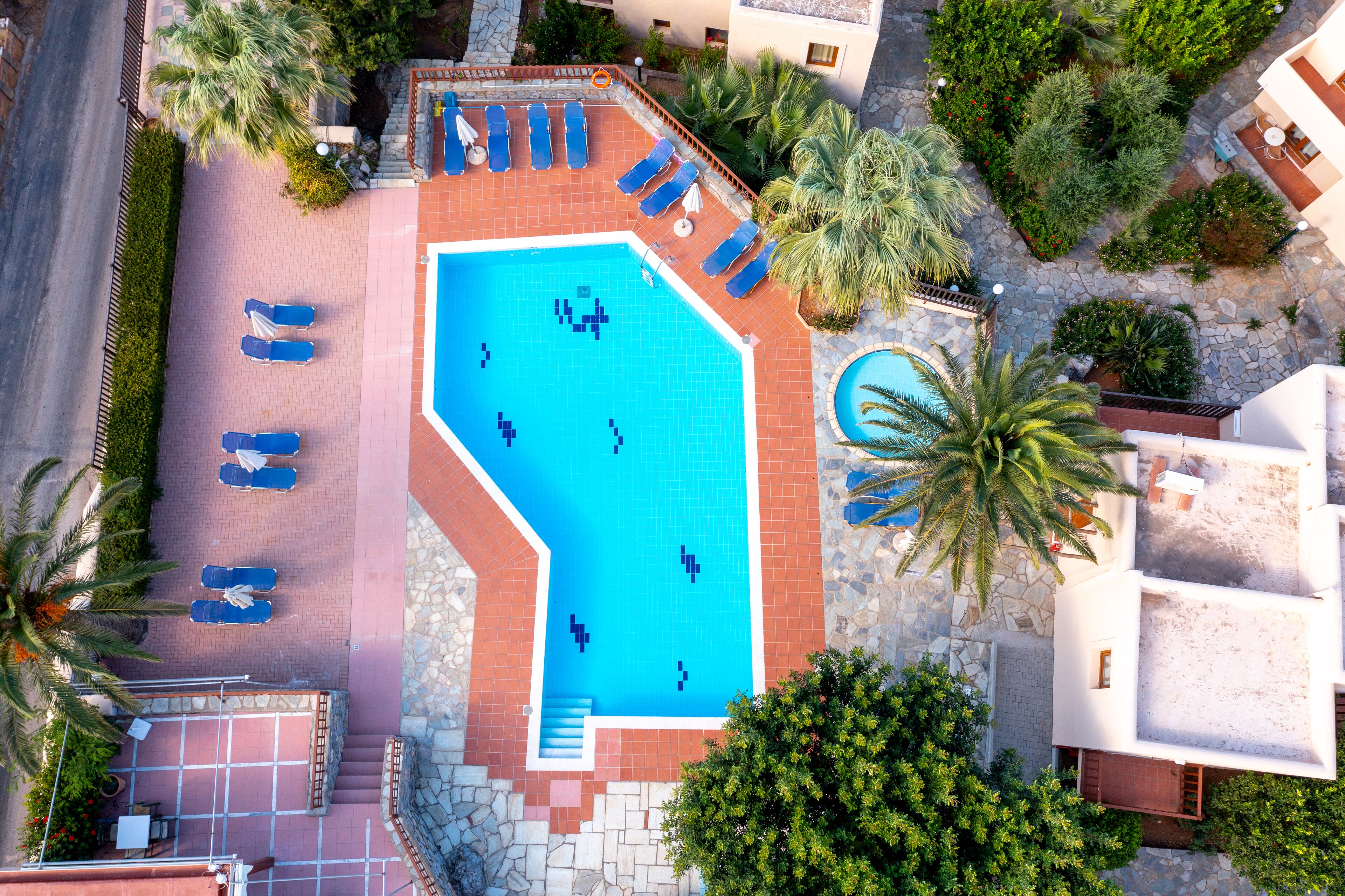 An aerial view of a hotel with a large swimming pool, sun loungers, and palm trees.