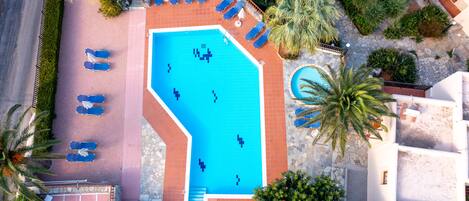 An aerial view of a hotel with a large swimming pool, sun loungers, and palm trees.