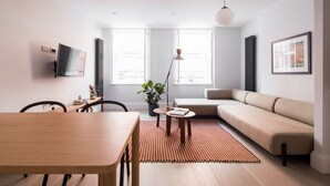 Uma sala de estar moderna com uma mesa de jantar de madeira, um sofá bege, um tapete vermelho estampado e um vaso com planta.