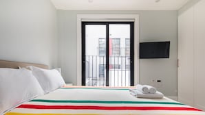 Quarto de hotel com uma cama grande, TV fixada na parede e vista da cidade pela janela.