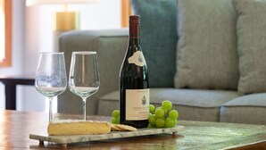 Una mesa con una botella de vino, dos copas, queso y uvas.