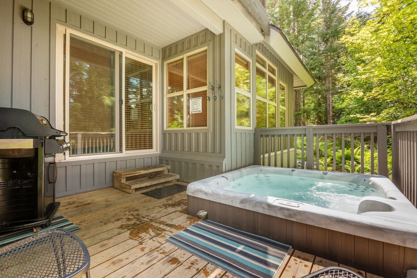 A wooden deck with a hot tub, a grill, and a covered seating area.