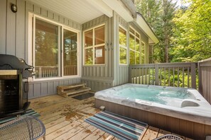 Une terrasse en bois avec un jacuzzi, un barbecue et un espace salon abrité.