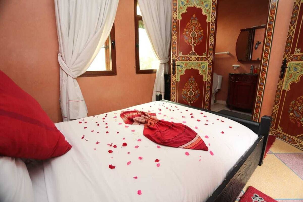 A bed with rose petals, a red pillow, and a person lying on the bed.