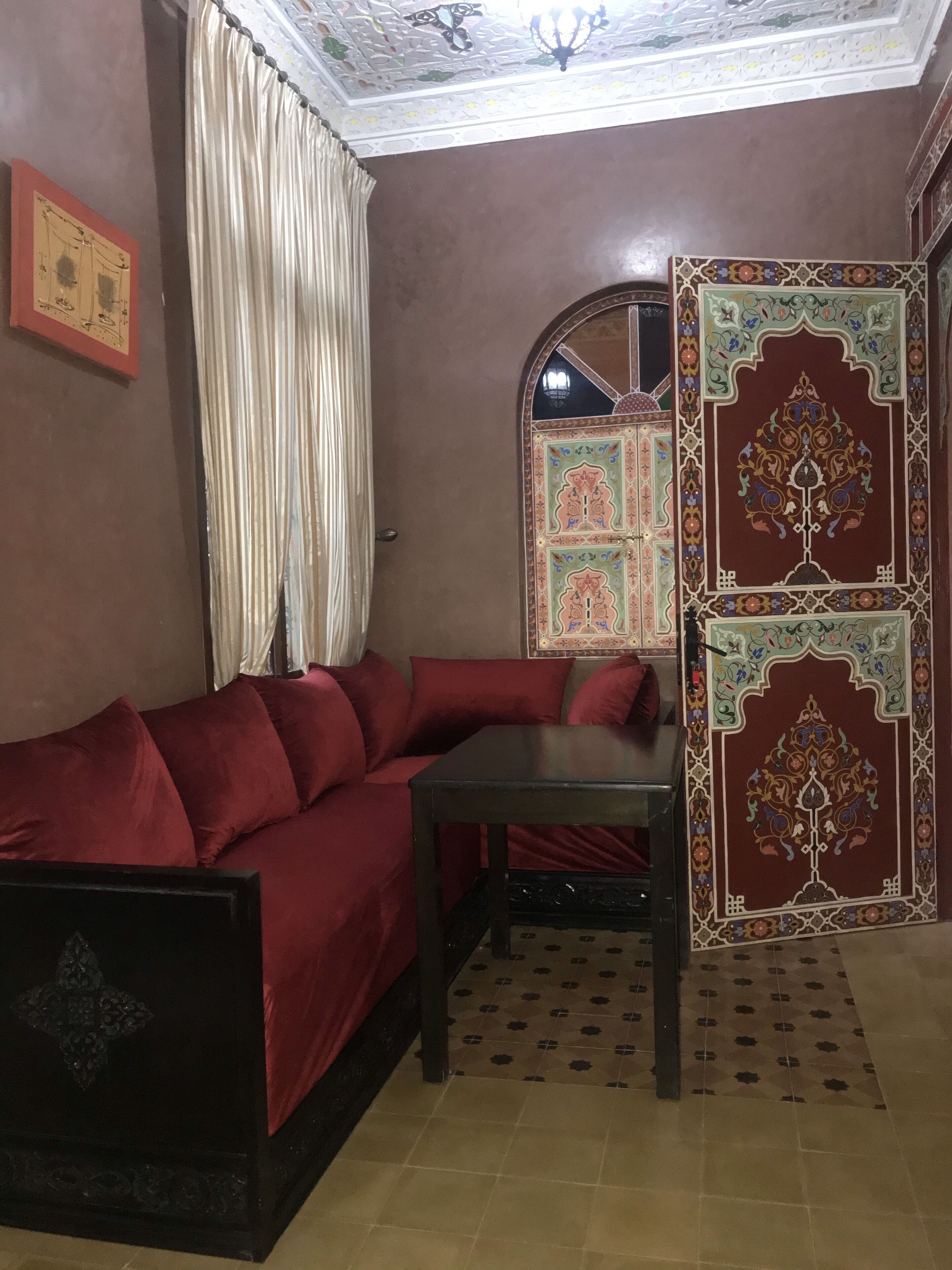 Una habitación con un sofá rojo, una mesita pequeña, un separador decorativo y un techo con diseños intrincados.