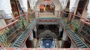 Un atrium à plusieurs niveaux, orné d’arcs blancs travaillés, une cour intérieure avec un sol à motifs et un balcon doté d’une balustrade.