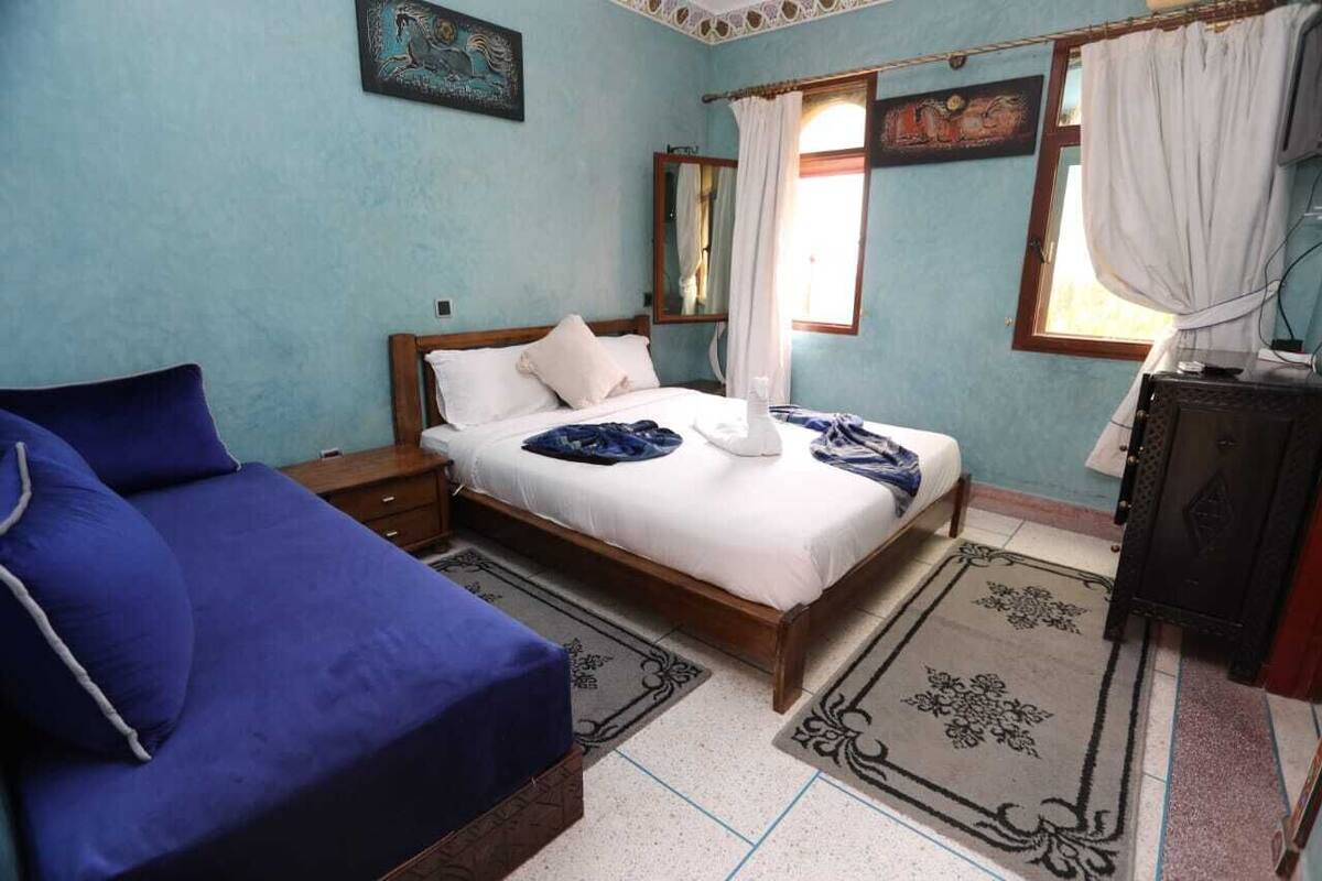 A bedroom with a bed, a nightstand, a dresser, and a window with curtains.
