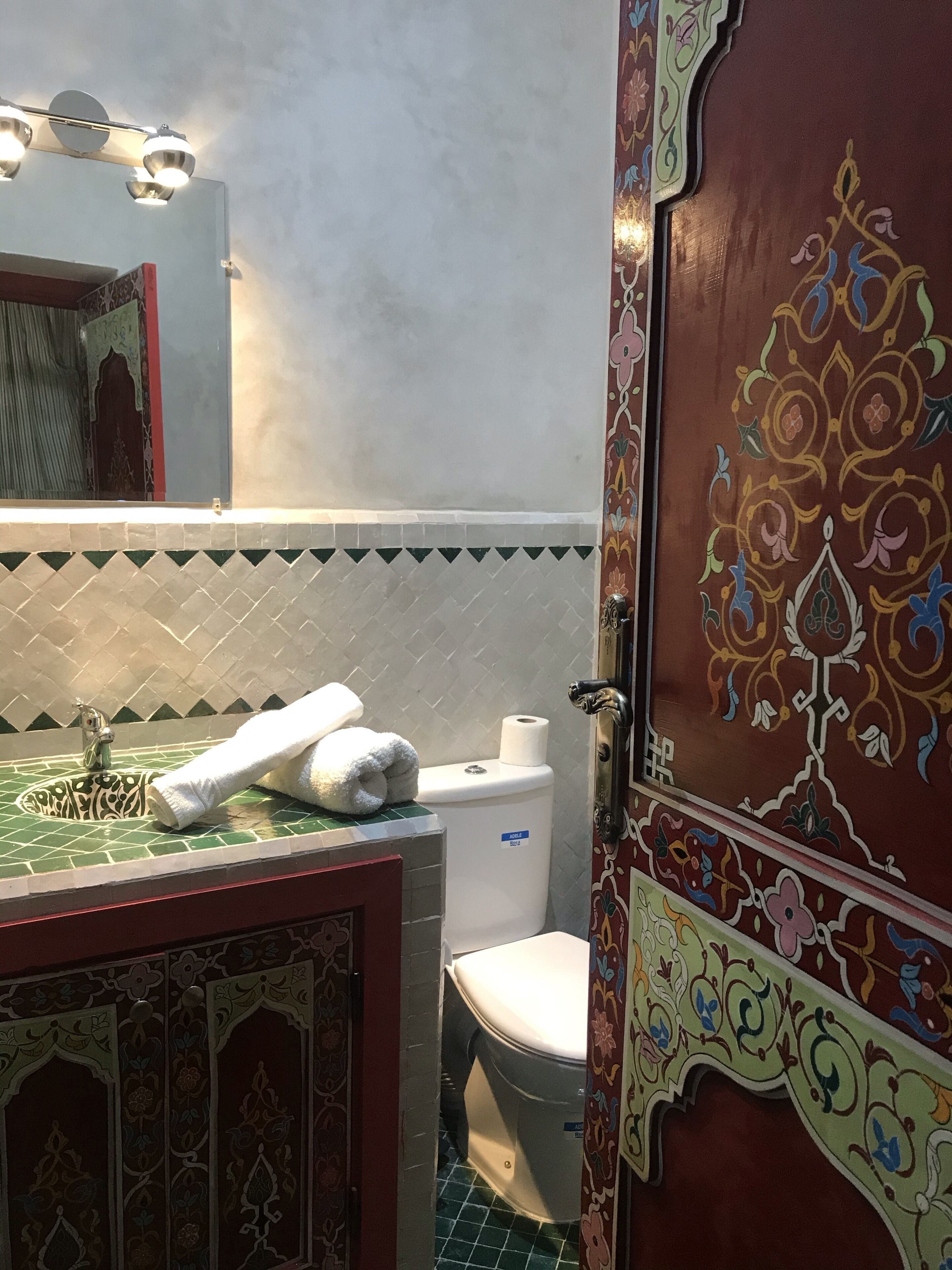A bathroom with a green tiled sink, a white toilet, and a decorative door with floral patterns.