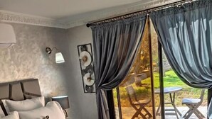 Une chambre avec un grand lit, une table de chevet, une lampe fixée au mur et une vue sur une terrasse extérieure.